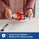 Hands holding a Dixie floral paper plate topped with a slice of cake over a textured table setting