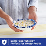 Person holding a Dixie Ultra blue swirl paper bowl filled with creamy soup over a striped tablecloth demonstrating soak-proof use.