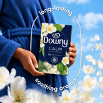 Hands holding a Downy CALM box in front of a blue sky backdrop with floral accents and aroma text