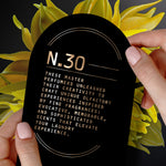 Two hands holding a black card labeled 'N.30' with descriptive copy over a background of yellow floral artwork