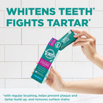Hands holding a tube and box of Tom's of Maine toothpaste in front of tiled background with large 'WHITENS TEETH FIGHTS TARTAR' headline.