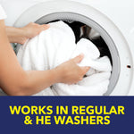 Close crop of hands placing a white towel into the drum of a front-load washing machine over a 'works in regular & HE washers' banner.