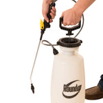 Hands operating the pump handle of a white Roundup garden sprayer with wand attached
