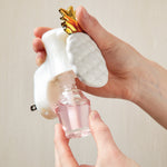 Two hands removing a pink fragrance refill bottle from a white pineapple-themed plug-in diffuser, showing bottle unscrewing action.