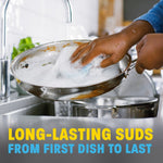 Close-up of hands scrubbing a soapy stainless steel frying pan at the sink, suds visible