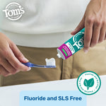 Close-up of hands squeezing Tom’s of Maine toothpaste onto a toothbrush over a sink, with a fluoride and SLS free badge visible.