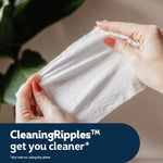 Close-up of hands stretching a white textured wipe to show material and cleaning ripples with product caption below