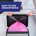 Hands pulling silver drawstrings to close a bright pink trash bag inside a stainless rectangular trash can