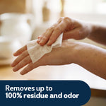 Close-up of hands using a textured wipe on the back of a hand with 'Removes up to 100% residue and odor' caption