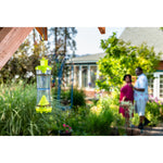 Hanging W-H-Y insect trap in garden foreground with two people blurred in the backyard scene