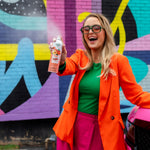 Cheerful person standing by a car holding a Citrus Magic Georgia Peach spray can against a vibrant mural