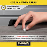 Hand placing a single white roach tablet on a floor next to baseboard with Harris logo and usage text banner above.