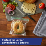 Top-down lifestyle image of a bagel sandwich inside a Hefty clear zip bag on a wood surface with sandwich ingredients nearby