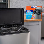 Kitchen scene with an open stainless trash can lined with a black Hefty trash bag and a Hefty product box on the counter.