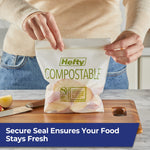 Pair of hands sealing a Hefty compostable press-to-close bag filled with apple slices on a cutting board