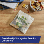 Hefty compostable snack bag on a wooden table near a backpack and bowl of trail mix, shown as on-the-go storage