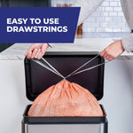 Hands pulling drawstrings closed on a peach-colored Hefty trash bag inside a countertop trash can, 'easy to use' label