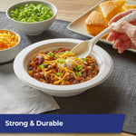 Hand holding a patterned Hefty ECOSAVE compostable spoon over a bowl of chili, tabletop serving scene