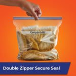 Hand holding a labeled Hefty gallon freezer bag filled with empanadas against orange background