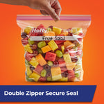 Hand holding a clear Hefty gallon press-to-close bag filled with fruit salad on an orange background