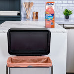 Open kitchen trash can lined with a peach-colored Hefty trash bag and the Hefty product box on the counter behind it