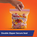 Hand holding a Hefty press-to-close quart bag filled with cherry tomatoes against an orange background