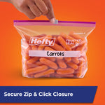 Hand holding a closed Hefty quart slider bag filled with baby carrots, labeled 'Carrots' against an orange background.