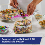 Hands spooning trail mix into a Hefty labeled quart slider bag with purple zipper on a kitchen counter.