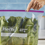 Close-up of a hand sliding the purple Hefty zipper closed on a clear bag containing leafy green lettuce