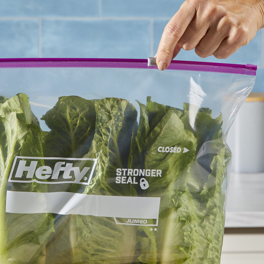 Close-up of a hand sliding the purple Hefty zipper closed on a clear bag containing leafy green lettuce