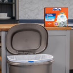 Kitchen scene with an open trash can lined with a white Hefty Ultra Strong bag and the product box on the counter