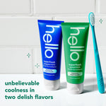 Two hello superfresh toothpaste tubes, blue peppermint and green spearmint, displayed next to a teal toothbrush on tile