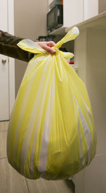 Hand holding tied yellow-and-white striped Hero trash bag demonstrating flap-tie closure in a kitchen