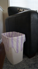 Small wastebasket lined with a purple-and-white striped Hero Scent Stripes trash bag beside a dark upholstered chair