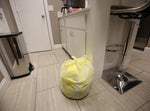 Tied yellow-and-white striped trash bag sitting on a tiled kitchen floor near cabinets and a stool