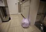 Tied purple-and-white striped trash bag on a tiled kitchen floor next to cabinets, matching Hero Scent Stripes design