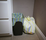 Small waste bin lined with a yellow-and-white striped HERO-style trash bag and a tied matching striped bag placed beside it.