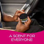 Pair of hands holding a California Scents 'Ice' air freshener can near a steering wheel in a vehicle interior.