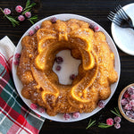 Baked holiday wreath cake on a white plate garnished with sugared cranberries and rustic table setting