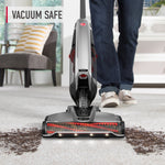 Front view of an upright Hoover vacuum cleaning carpet with visible brush roll and ‘vacuum safe’ text overlay