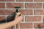 Hand connecting tan misting tubing to an outdoor brass faucet fitting mounted on a brick wall.