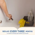 Hand placing a small bait station inside a cabinet shelf next to cleaning gloves and bottles illustrating placement