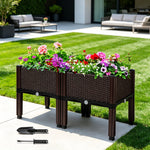 Woven-style elevated planter on legs filled with colorful flowering plants on a patio, small gardening trowel and fork beside it.