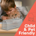 Clear plastic humane mouse trap on a table with a small rodent inside and a blurred child and cat in the background, labeled child & pet friendly
