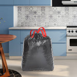 Lifestyle-style image of a filled black Husky drawstring trash bag standing on a kitchen floor in front of cabinets