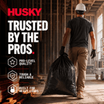 Construction site lifestyle image of a worker carrying a full black trash bag with Husky logo and product benefit icons