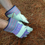 Gloved hands wearing gray leather-palm work gloves handling pine needles in an outdoor setting