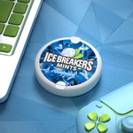 Lifestyle scene with an Ice Breakers coolmint puck on a blue textured surface beside a game controller and laptop