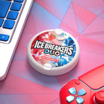 Lifestyle desk scene with an Ice Breakers Duo strawberry tin placed on a pink geometric surface next to a laptop and controller