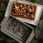 Baked loaf with piped white icing showing Santa sleigh design alongside the matching Nordic Ware loaf pan